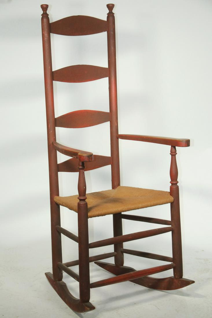 EARLY LADDERBACK ROCKING CHAIR: 18th c. Red Painted Ladderback Rocker, with rush seat, four slat back, shaped and scrolled arm rests, found in southeastern CT, 48 3/4" high, 22 1/4" x 22 1/4". Paint losses, surface wear.
