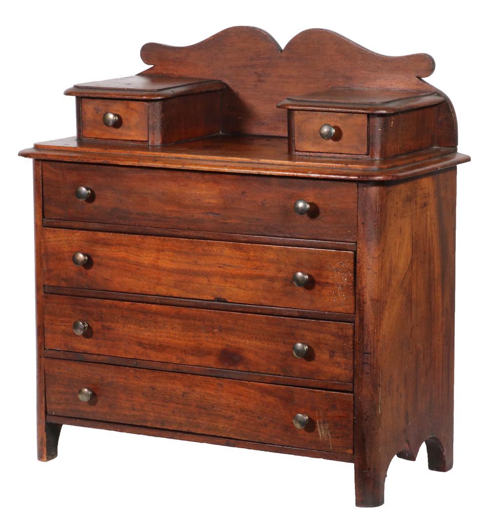 DOLL SIZED VICTORIAN WALNUT CHEST: Bench Made Miniature Chest of Drawers with tall shaped backsplash, two setback glove drawers, molded overhanging tops, four drawers in the case, all with brass button pulls, raised on square legs with