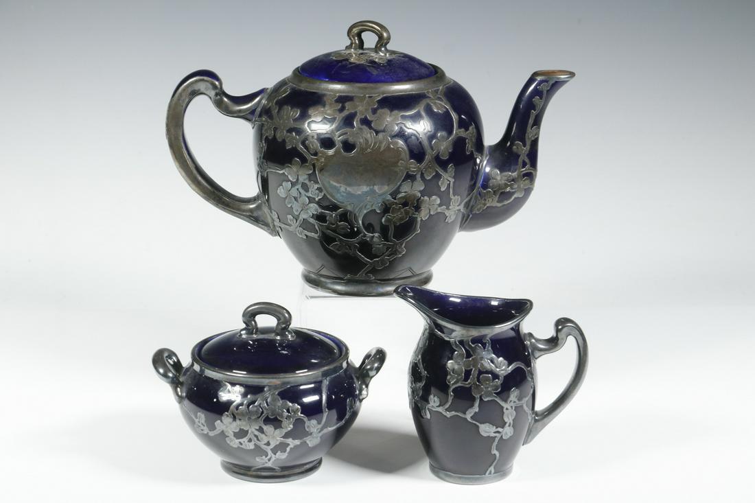 (3 PC) LENOX ART NOUVEAU SILVER OVERLAY TEA SET: Circa 1905 (3)-Piece Tea Set by Lenox, with floral design silver overlay on a cobalt blue glazed surface, incl: Teapot, 6" high, 9" x 5"; Creamer, 4" high, 4" x 2 1/2"; and Lidded sugar bowl, 3 1/2" h