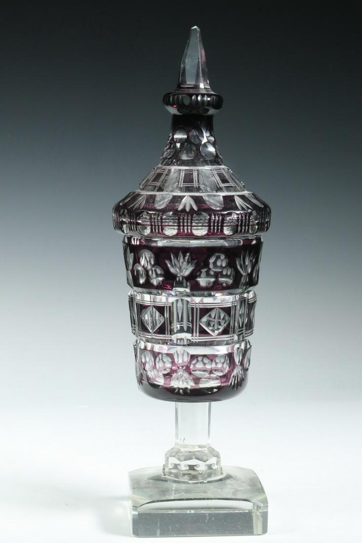 CUT CRYSTAL LIDDED POKAL: Large Late 19th c. Purple Flashed Cut Crystal Lidded Chalice, probably Bohemian, with geometric cut patterns, set on a heavy square clear beveled edge base, 14 3/4" high, 4 1/2" diam. Old metal base b