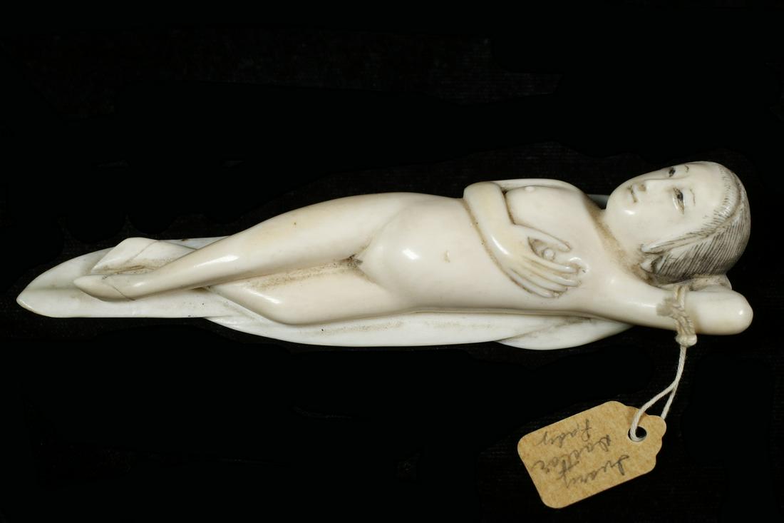 19TH C. CHINESE "DOCTOR'S LADY": Carved Reclining Woman, one arm behind her head, the other with hand to her breast, her legs crossed, shoes on bound feet, laying on a cloth, unsigned, 4 5/8" long. Old collector's tag attached.