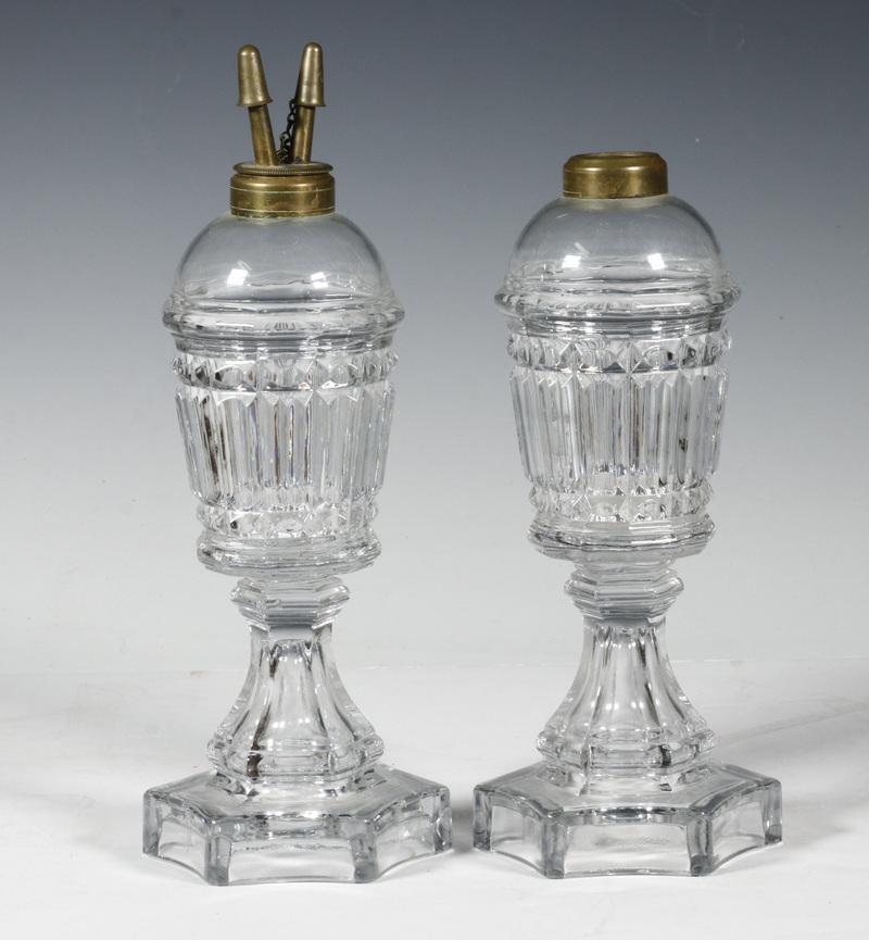 PR OF FLINT GLASS WHALE OIL LAMPS: Pressed Prism Flint Glass. circa 1840, probably manufactured at The Boston and Sandwich Glass factory, with ribbed sides and a six sided base. 8 5/8" tall without font. One font cap is missing.