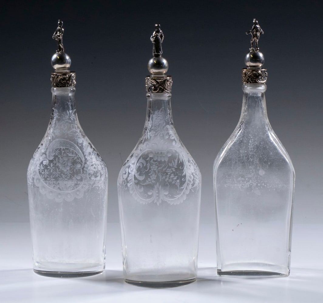 (3) GERMAN SILVER MOUNTED ETCHED GLASS BOTTLES: (3) GERMAN SILVER MOUNTED ETCHED GLASS BOTTLES Lot of (3) Late 19th c. Shaped Liqueur Bottles, with fancy etched decorated shoulders, with silver collars and silver topped figural stoppers, all