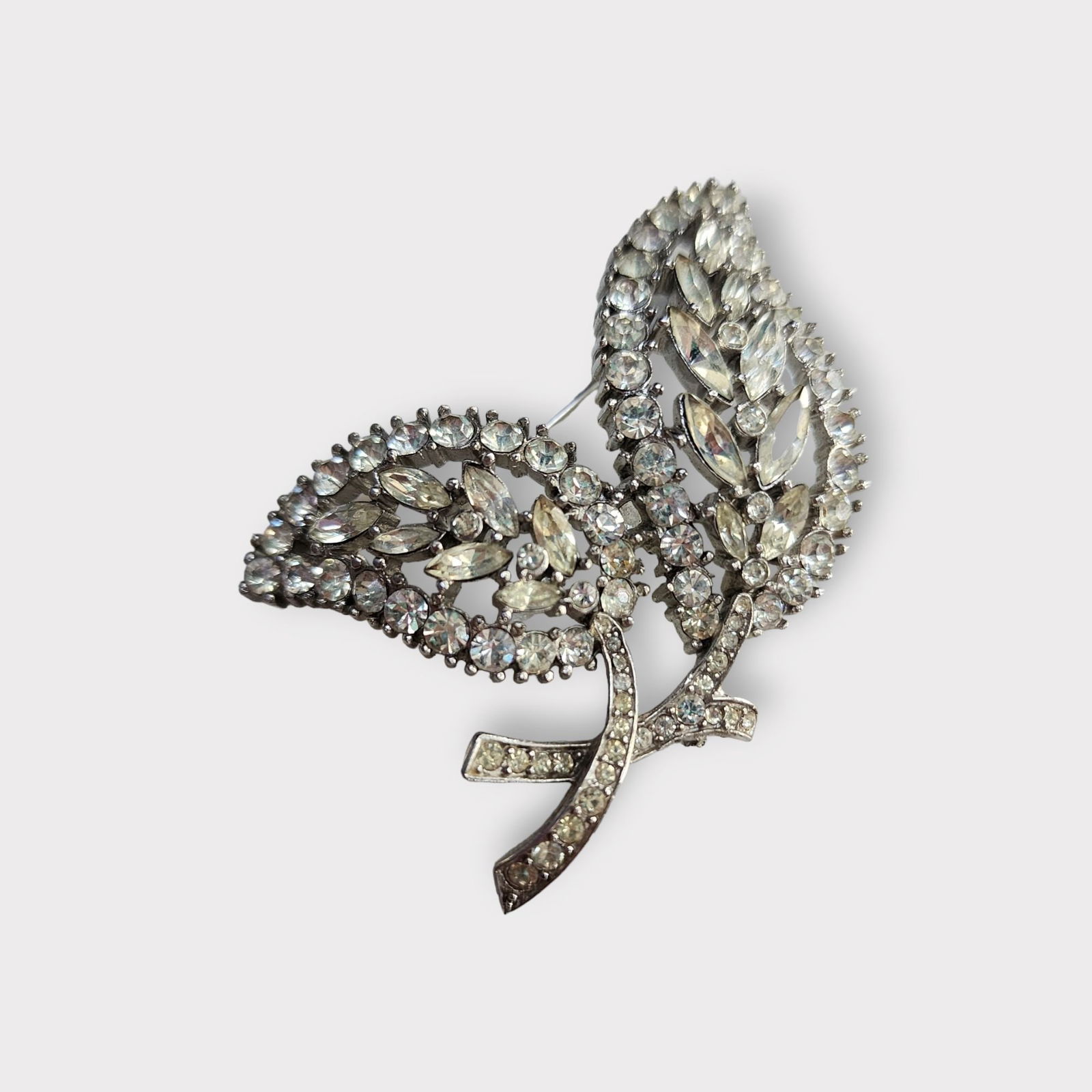 VINTAGE TRIFARI SIGNED RHINESTONE LEAF BROOCH: Vintage Trifari Signed Rhinestone Leaf Brooch Size: 2.25"Color: Clear, SilverCondition: Very good condition Signed: Trifari Details: Marked with the crown. WE PROVIDE FREE IN-HOUSE SHIPPING WITHIN THE