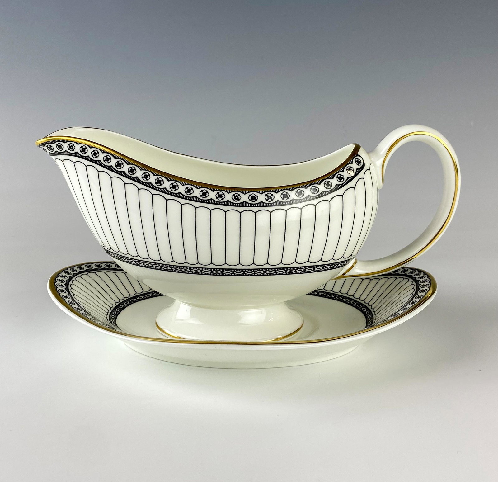 Wedgwood China Colonnade Gravy Boat and Underplate: Wedgwood (English). Black geometric line design with circles around border, rim with a gold trim. Pattern introduced 1960, retired 2004. Warm glazed finish. Signed with black urn stamp WEDGWOOD BONE C