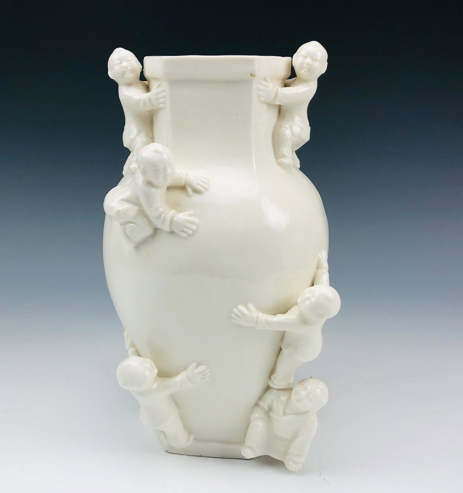 Chinese Blanc De Chine Porcelain Vase w/ Children: Uniquely modeled Chinese porcelain vase with a hexagonal mouth opening over a low sloped shouldered tapered body. Features young children in robes merrily crawling around. The glazed finish and nice d