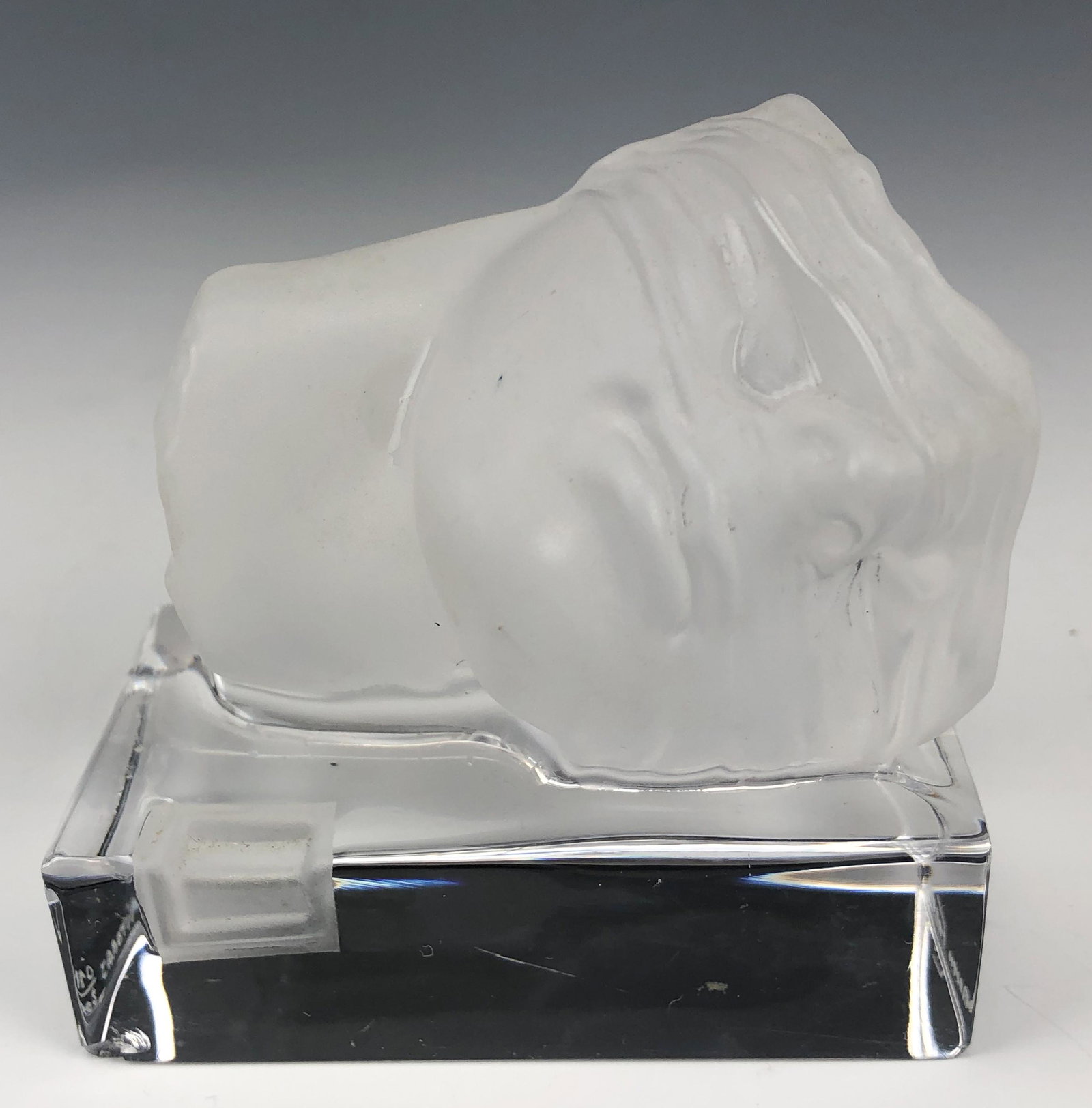 Daum France Mitoraj Surrealist Crystal Sculpture: Features a modern colorless pate de verre crystal Surrealist figural sculpture of a blindfolded fragmented face laying on it's side on a rectangular glass base. Designed by the German Polish sculpture