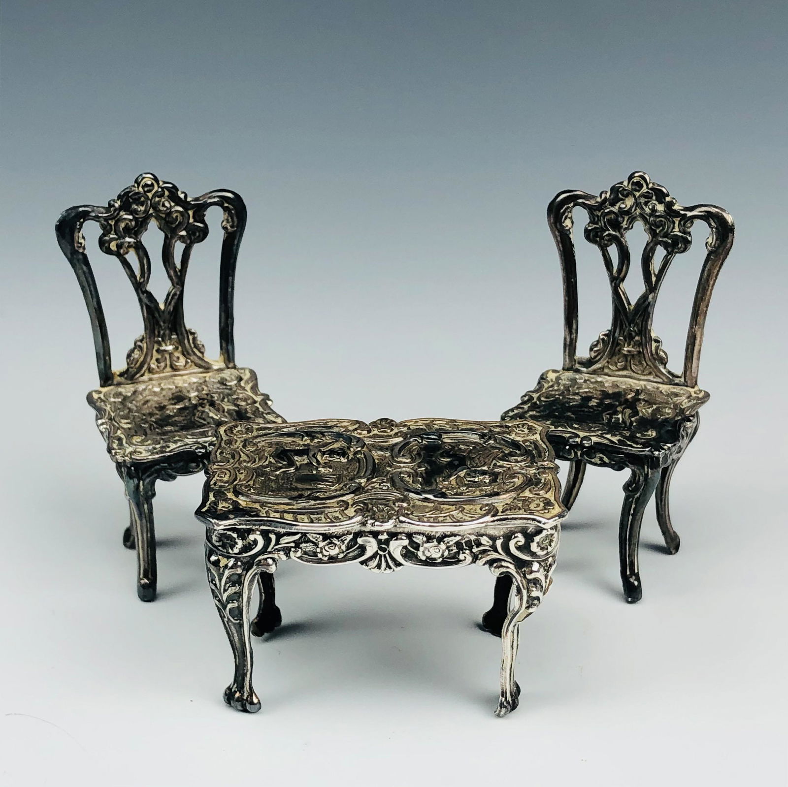 English Sterling Mini Doll House Chairs Table Set: Exceptionally well crafted articles of English Sterling Silver artistry of miniature proportions. There are a pair of dining chairs and a card table. All feature the mythological heavenly nude angel c