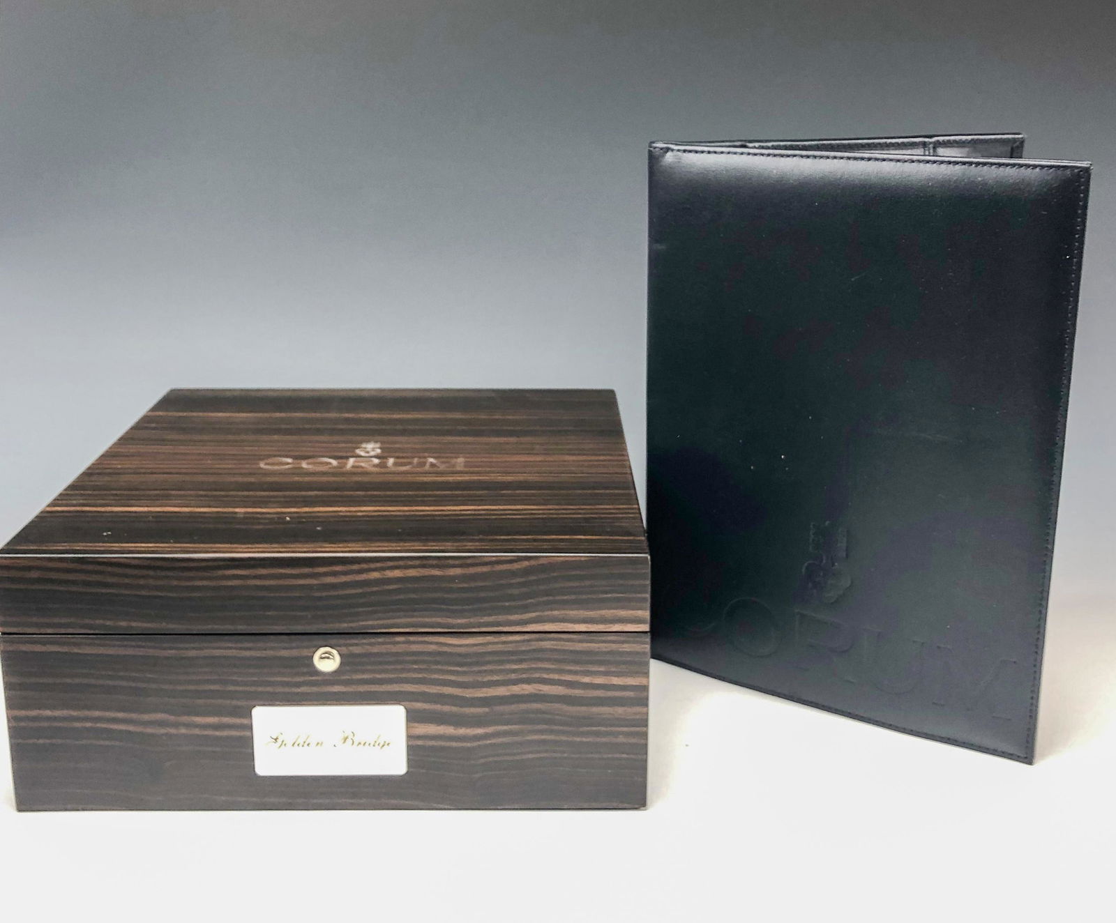 Corum Golden Bridge Presentation Watch Box Book CD: Corum Presentation Watch Box for the Golden Bridge Model Luxury Wrist Watch. Preowned. Constructed of precious wood with glass mirrored interiors and black suede padding. Watch support form in the sha
