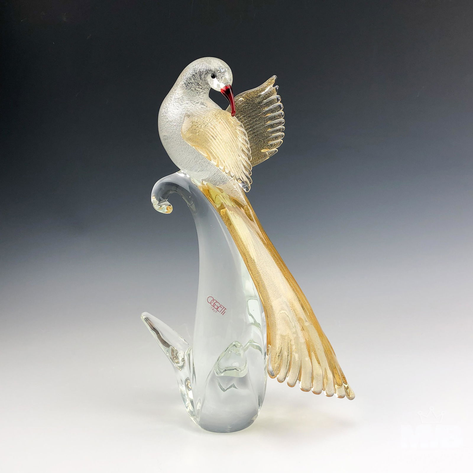 Murano Oggetti Italian Art Glass Bird Figurine: Murano bird figurine by Oggetti. Features a red beaked clear glass bird of paradise with incased gold flaked wings perched atop a clear glass foundation. Good overall condition with mild storage wear.