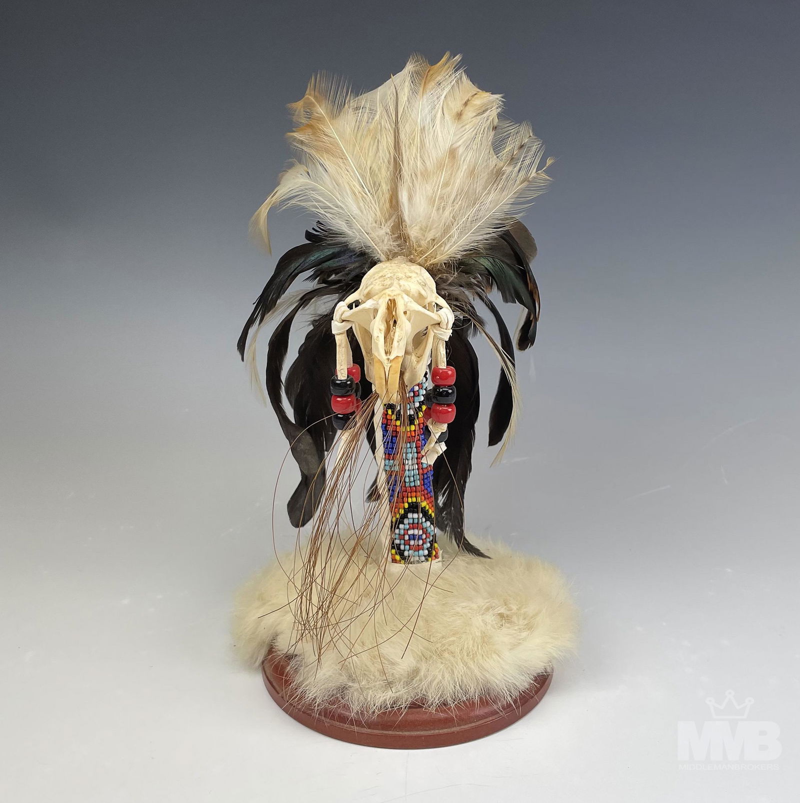 Native American Indian Trial Fetish Art Sculpture: Sculpture depicts a animal skull with feathers, exquisite beadwork patterns and hair fur in the Native American style. Mounted to a wood base. Signed on bottom. Measures 9 in x 5 in x 5 in. Good overa