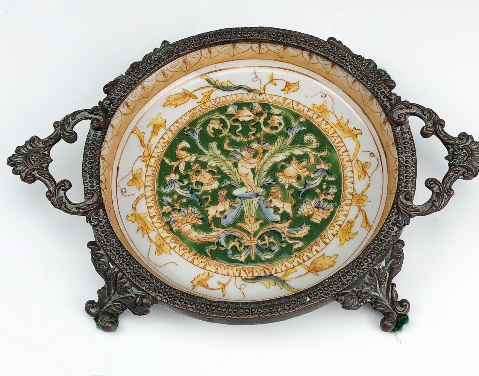 Wong Lee Chinese Brass Porcelain Enameled Coaster: Wong Lee 1895 wine bottle coaster. Four post legged brass coaster with a porcelain center. Center is a hand painted Chinese design centered around a cherub. Marked on bottom. Good overall condition wi