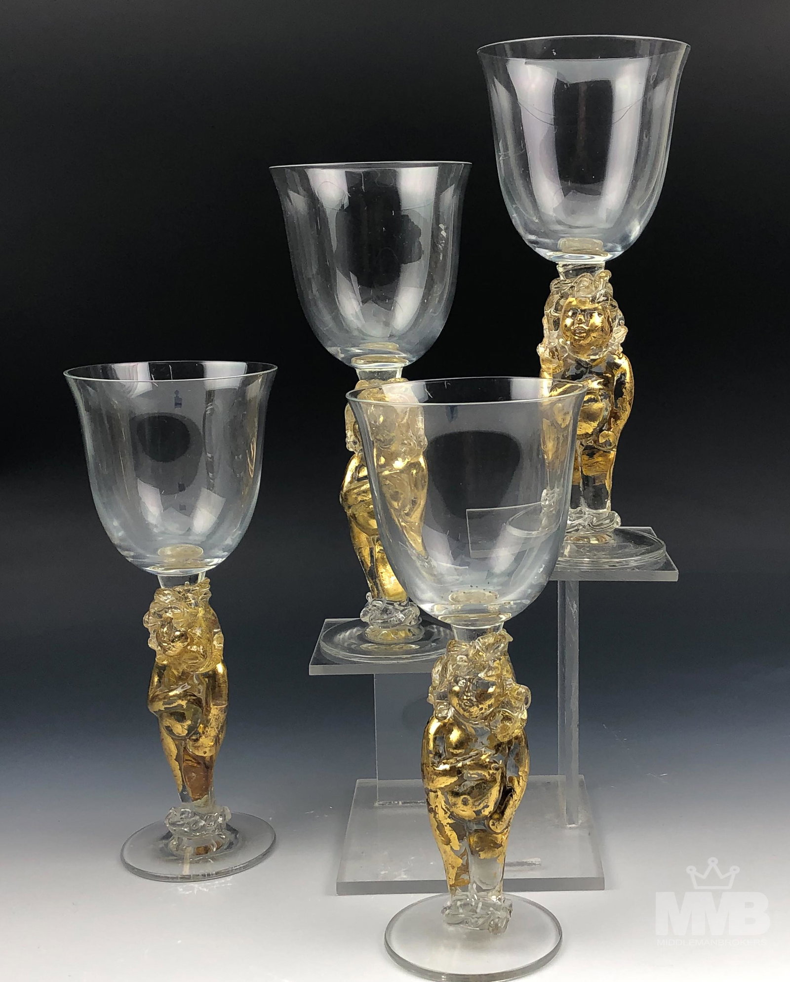 Tony Davlin Nude Cherubs Studio Art Glass Goblets: Signed set of four Tony Davlin Studio Hand Blown Art Glass Goblets. Each stem features the mythological nude cherub angel with applied gold leaf supporting a clear bowl above. Good condition. No chips