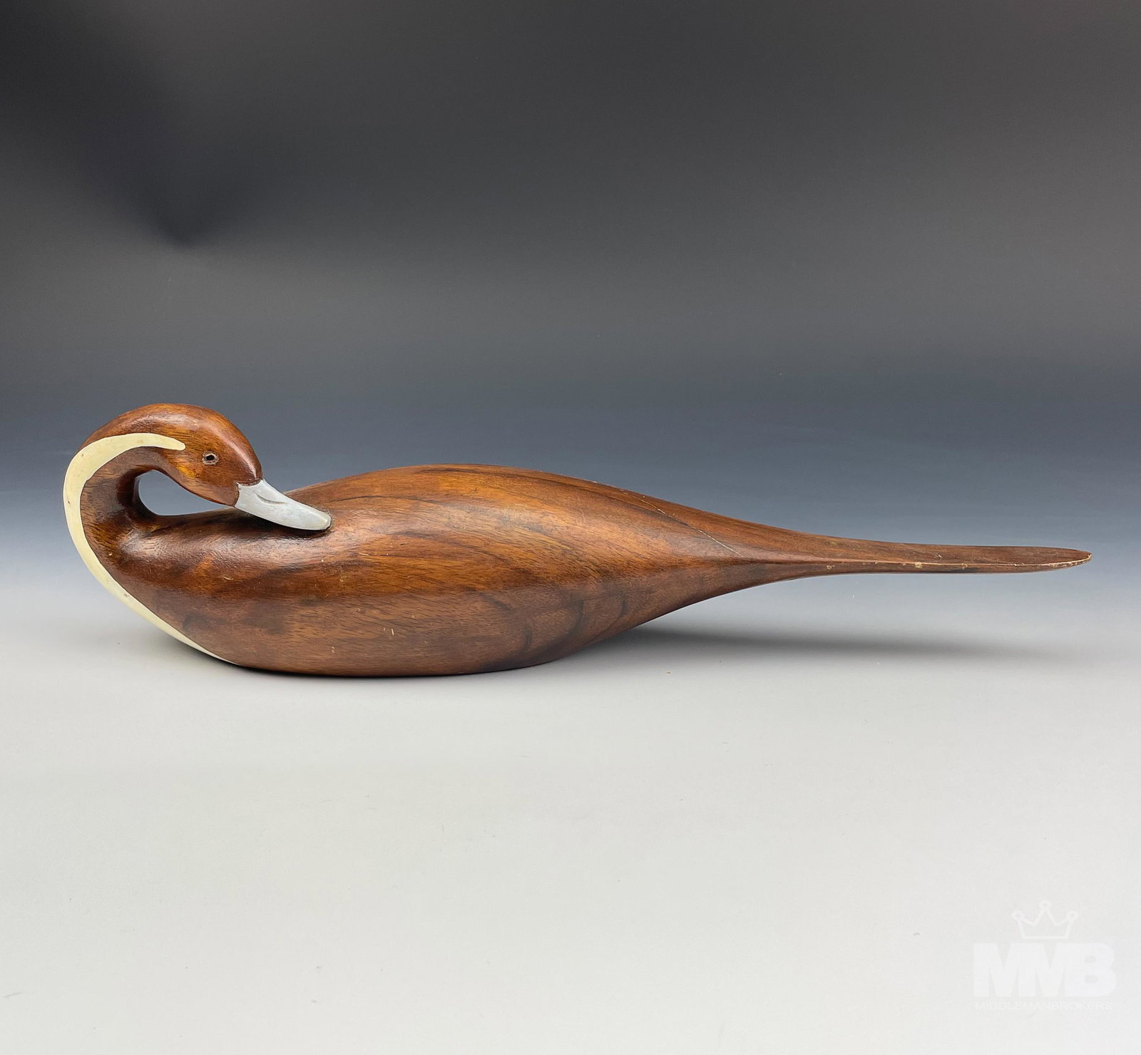 Mid Century Modern Carved Wooden Duck Sculpture: Features a long tailed duck in seated / resting pose, with white breast extending over to the neck on opposite sides and having a pale grey colored bill. Warm naturalistic colors and graining seen in 