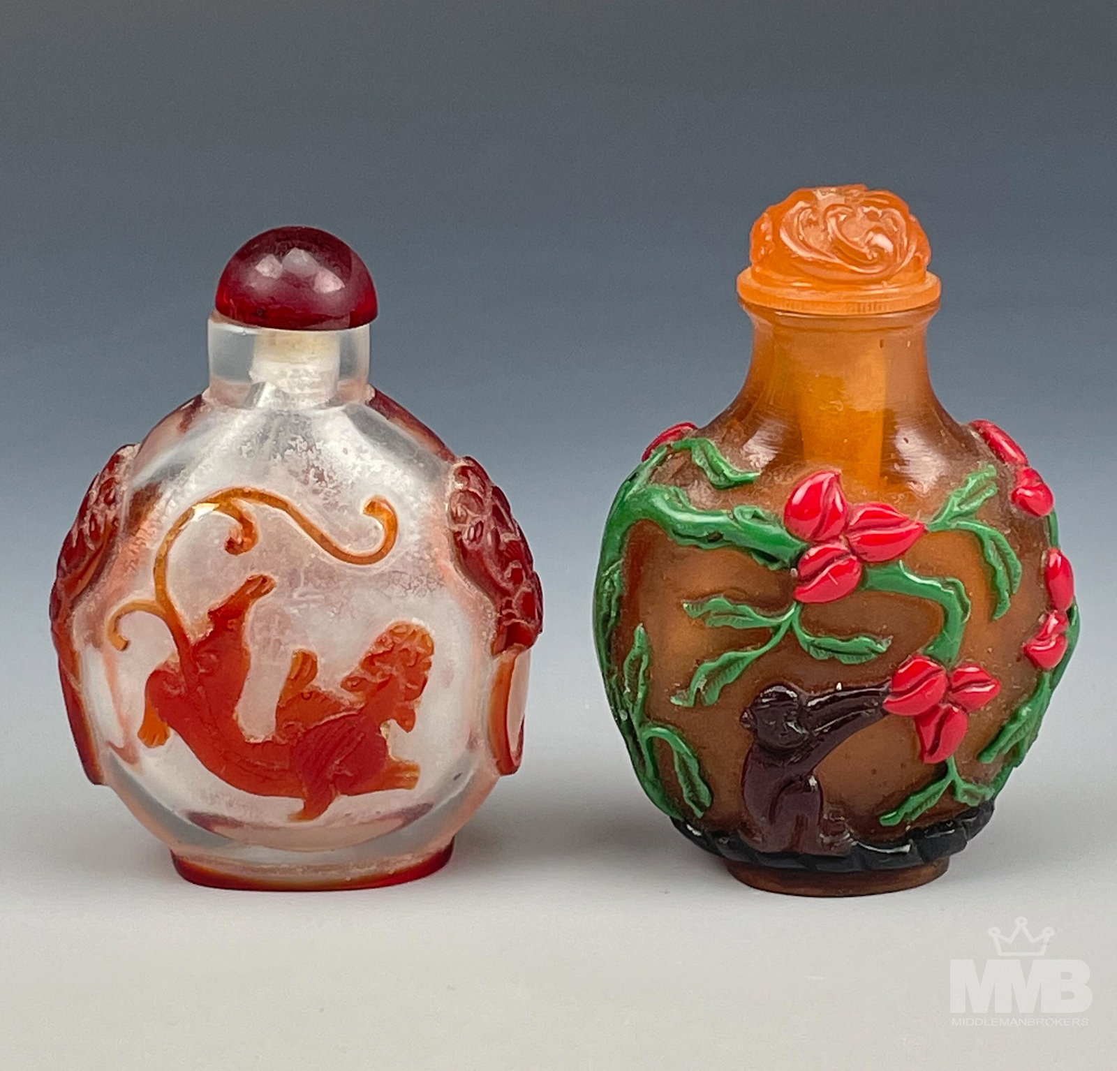 2 Chinese Overlay Carved Peking Glass Snuff Bottle: Features Chinese Origin Peking Glass Snuff bottles one depicting monkeys eating from fruit trees, the other features a mythological animal on opposite sides, the adjacent sides with lion mask faces. D