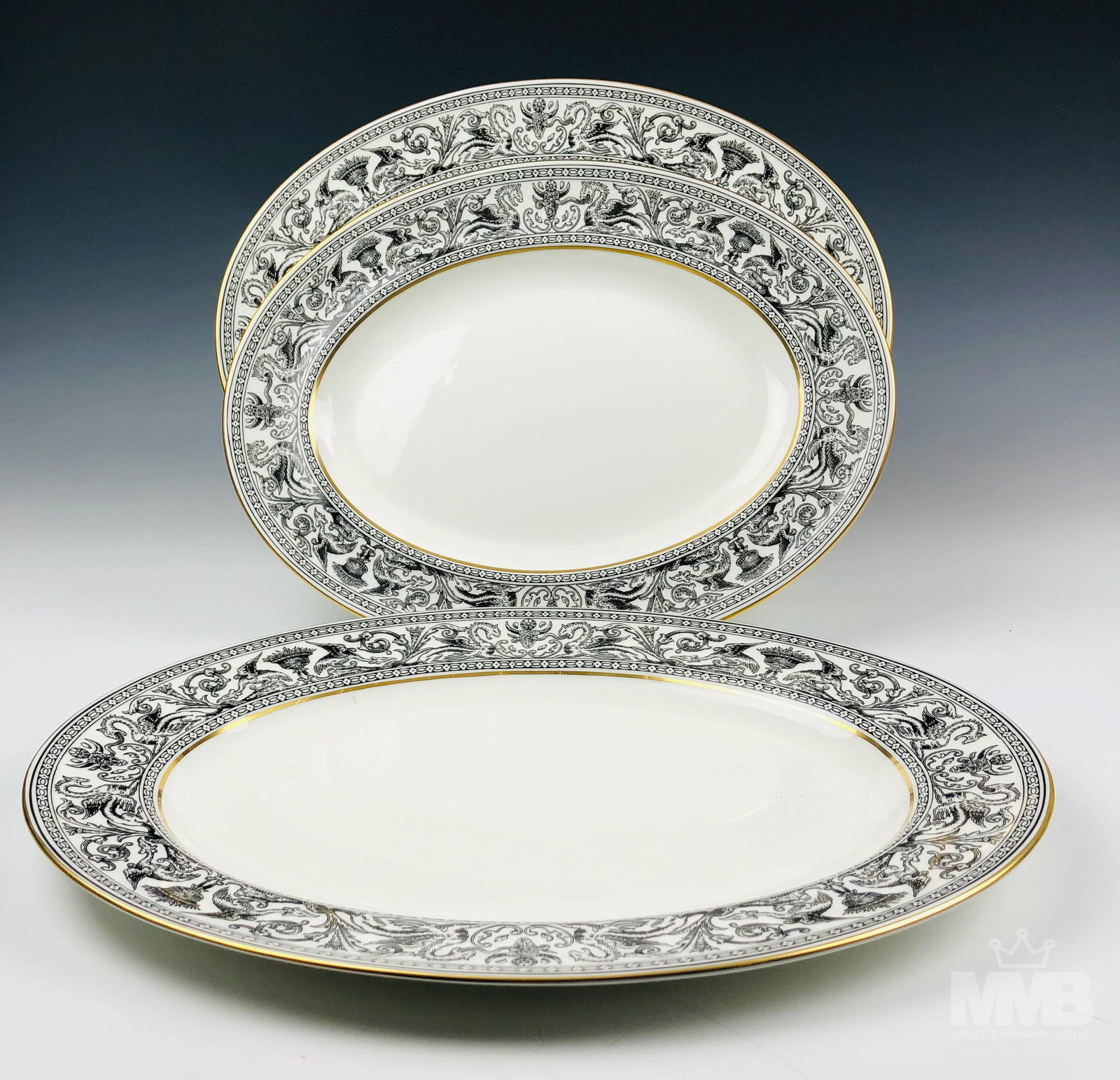 3 Wedgwood Florentine Black Oval Serving Platters: Each graced with mythological dragons, phoenix birds and floral decorations around the border, against a crisp white ground with gold trimmed linings. Production years 1959 - 1997. Glazed finish. Good