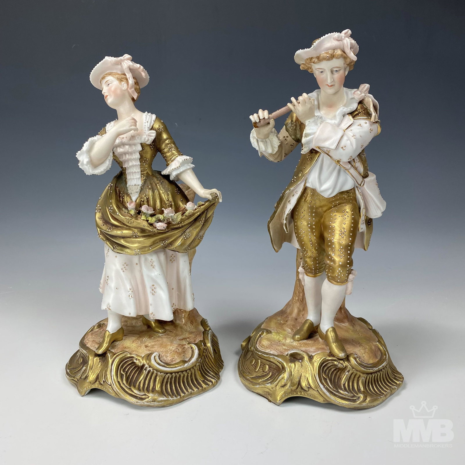 Pair of German Porcelain Man & Woman Figurines: Pair of German porcelain figurines. Hand painted in white and gold gilt featuring a man playing the flute and a woman dancing. Marked "S" on bottom. Good condition with minor wear and loss to paint. M