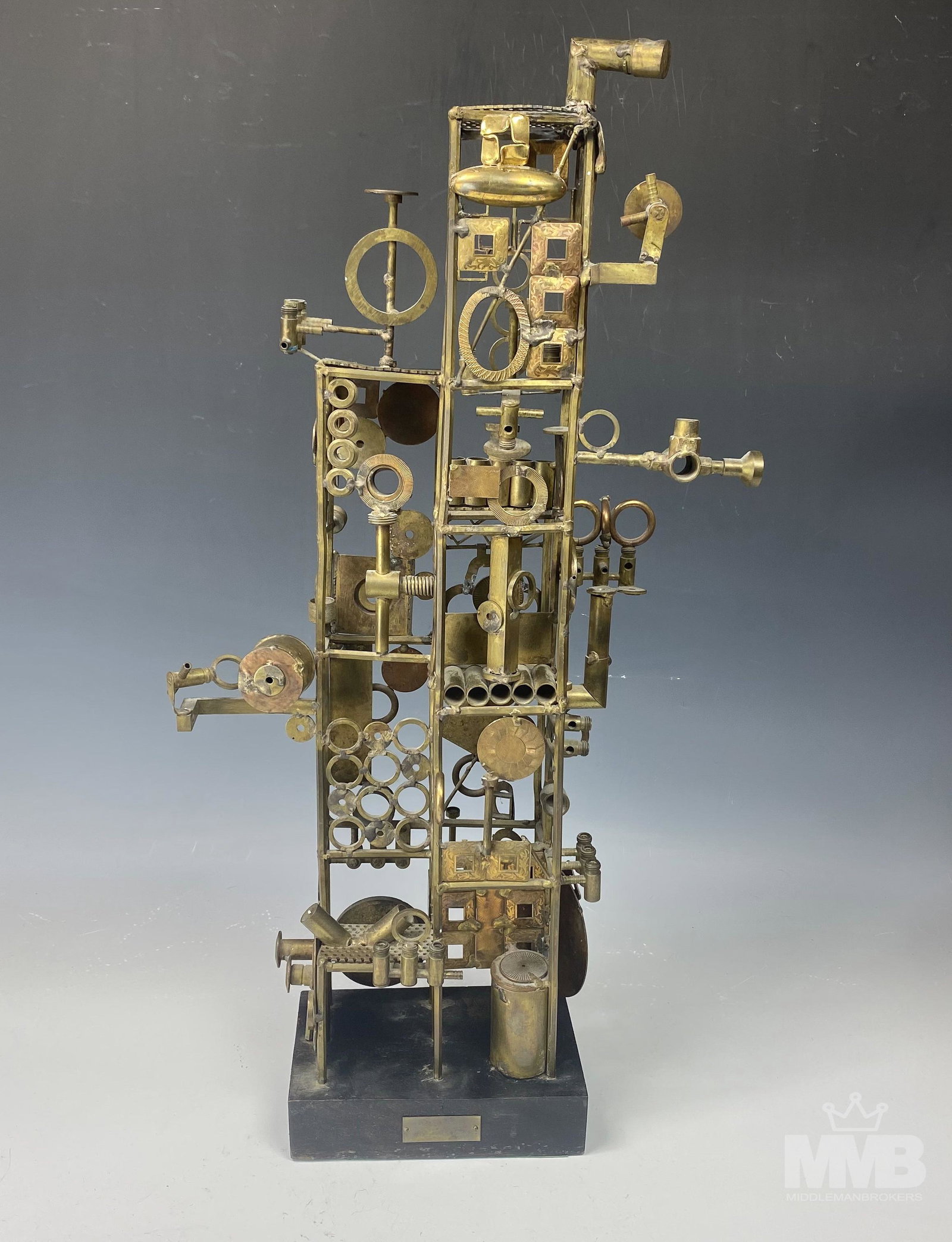 H W Hauptman Mid Century Modern Metal Sculpture: Features an arrangement of various brass metal hardware objects forming a complex design. Mounted atop a black colored rectangular wooden base. Signed on the metal plaque lower front center base. SHIP