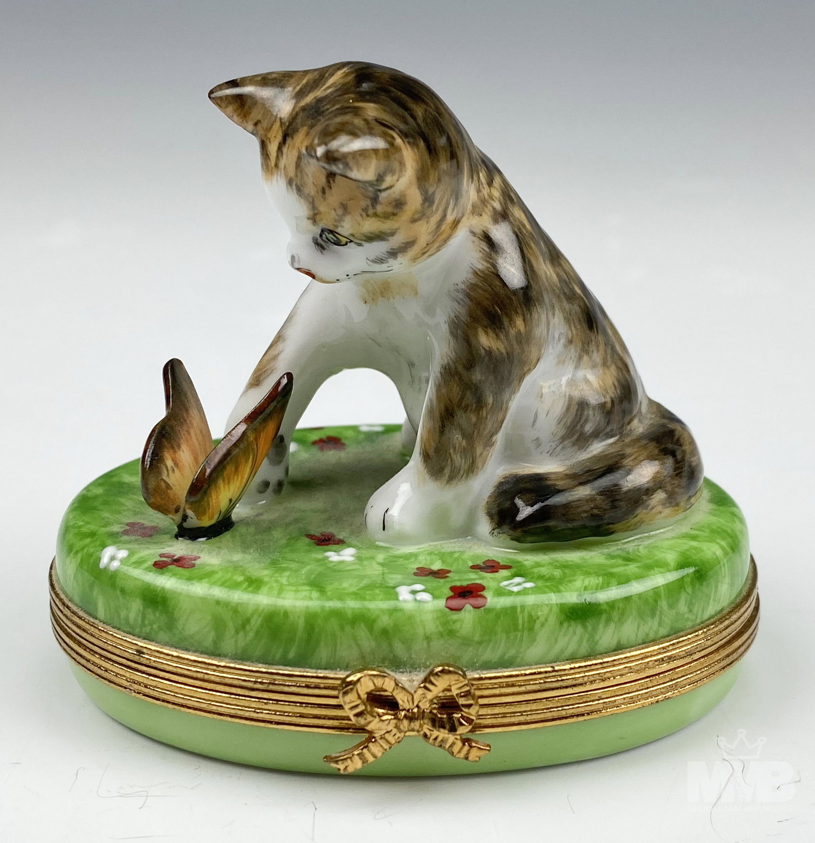 Rochard Limoges Kitten Butterfly Trinket Coin Box: Features a hand painted porcelain striped kitten seated on a grass bed with colored flowers, inquisitively looking at his winged friend that has come to visit him. Gilt brass mounted hardware around t