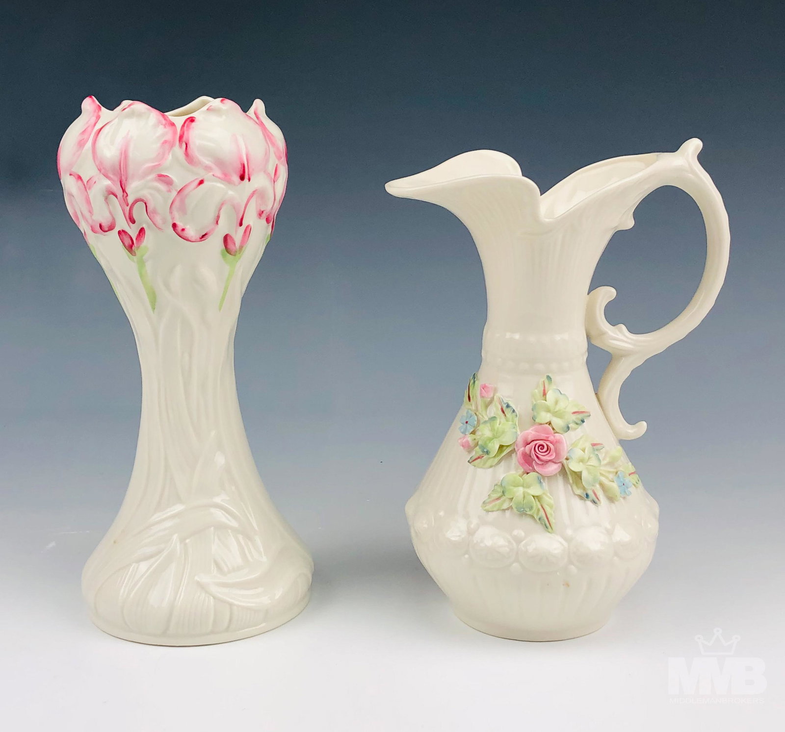 Lot 2 Belleek Irish Porcelain Floral Mantle Vases: The jug shaped vase graced with an applied pink rose, blue flowers and green shamrocks on one side of the body with raised oval daisy flower pattern running around the base with vertical ribs below. T