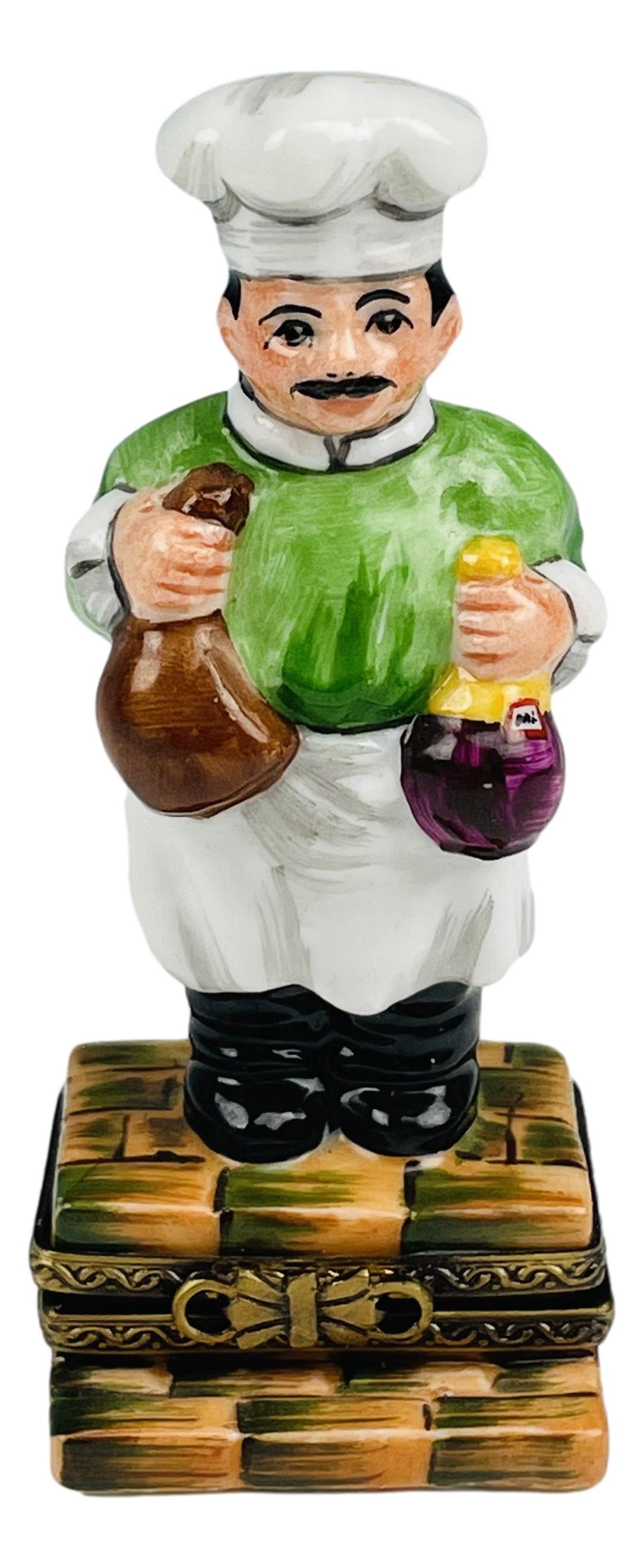 Limoges French Porcelain Chef Cook Trinket Box: Features a chef / cook holding a brown bag in one hand, a wine bottle in the other. Bow style gilt brass hardware clasp closure. Glazed finish. Signed with artist signature Elda Creations Fabrique et