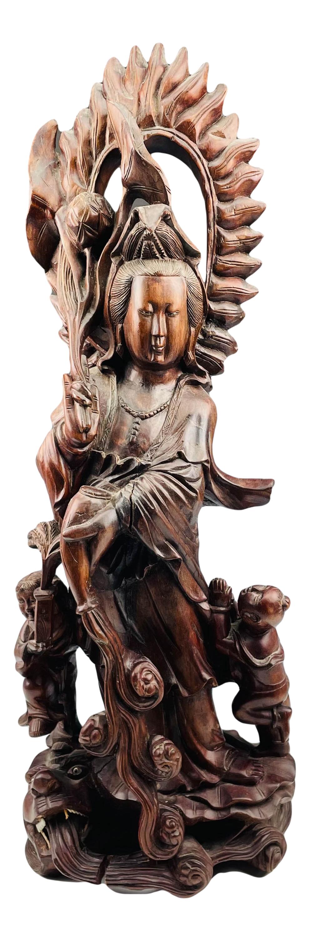 Chinese Export Buddha Child Demon Wood Sculpture: Features the revered deity God Buddha in standing pose with a flaming halo around his head, holding articles in each hand, with a child on each side and standing atop a demonic face with a fish scale 