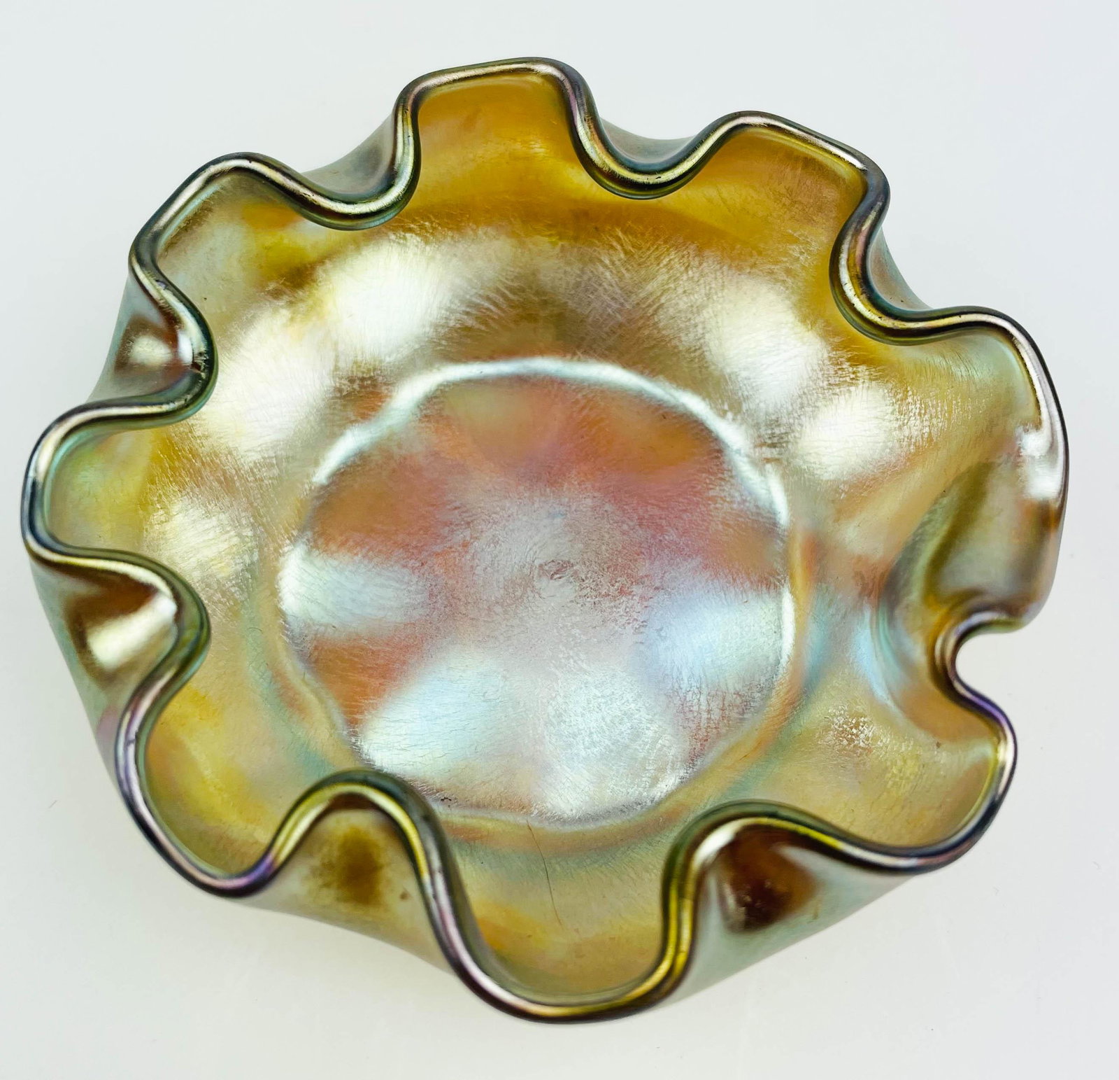 Tiffany Style Gold Iridescent Ruffled Glass Dish: Early 20th century studio hand blown art glass nut candy dish bowl. Graced with a ruffled / crimped border with a gold iridescent coloration. Measures 2 3/4". No apparent markings or signatures. Dimen