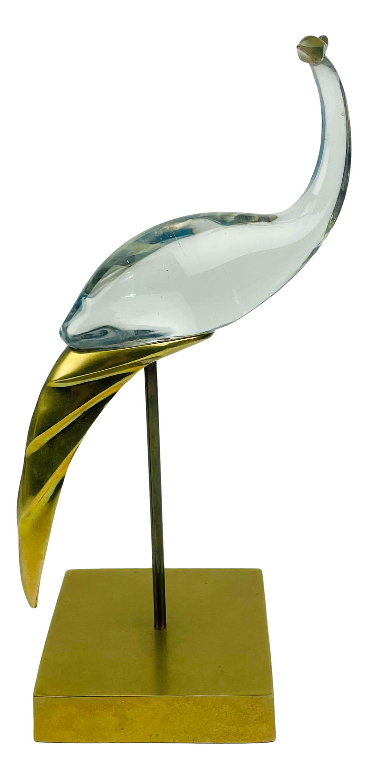 Hollywood Regency Glass Brass Stork Bird Sculpture: 1980's era mixed media nature inspired home decor sculpture. Depicts a stork heron bird with a clear glass body with mounted brass accents to the head and the tail. Surmounted on a brass stand screwed