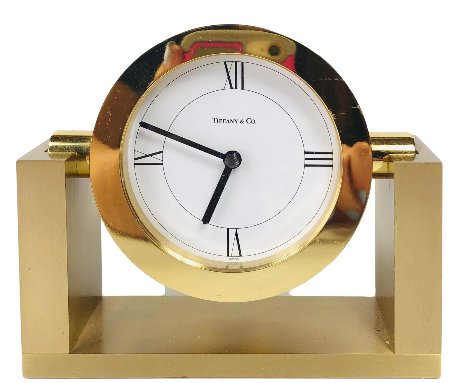 Tiffany & Co Contemporary Round Brass Desk Clock: Contemporary design brushed and polished brass desk clock by Tiffany & Co. White face with Roman numeral markers. Round face swivels in bracket style base. Swiss quartz battery powered movement. Face 
