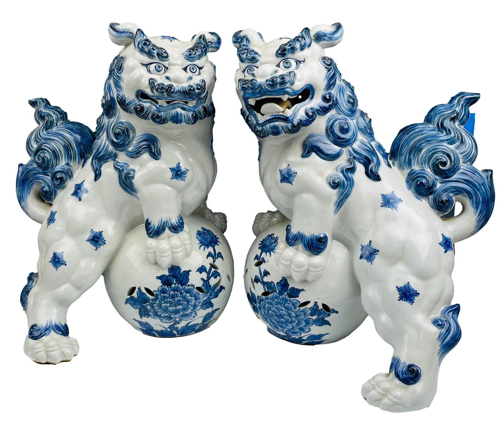 Chinese Export Blue & White Porcelain Foo Dogs PR: Pair of late 20th century Chinese export opposing porcelain palace foo dogs. Featuring a blue and white glazed finish, with numerous curled tufts, and large teeth with tong grins. Each balanced on a s