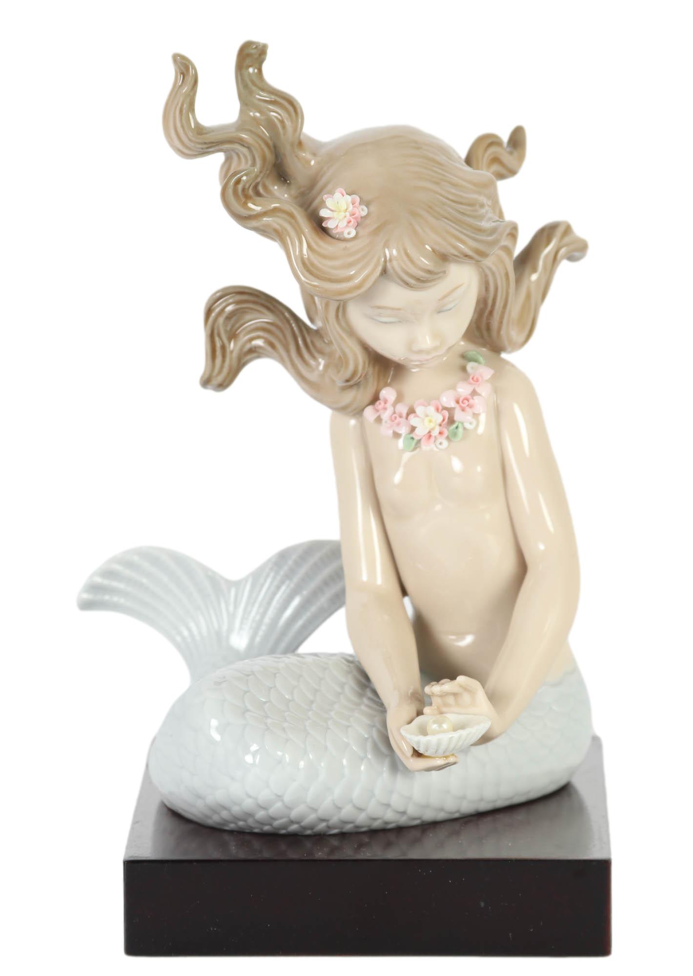 Lladro Mirage # 1415 Porcelain Mermaid Figurine: Designed by sculptor Jose Puche. Issued in 1982. Features this mythological being in gloss finish in seated pose holding a shell in her hand with a pearl in it, flowers adorning her long wavy hair. Si