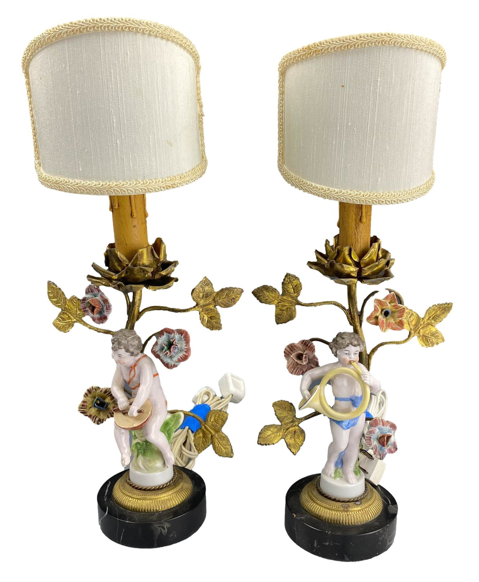 Antique Porcelain Cherub Musician Gilt Brass Lamps: Pair of early 20th century European origin porcelain and metal table desk lamps. Each features the legendary mythological nude angel playing a musical instrument, the gilt brass hardware forming the s