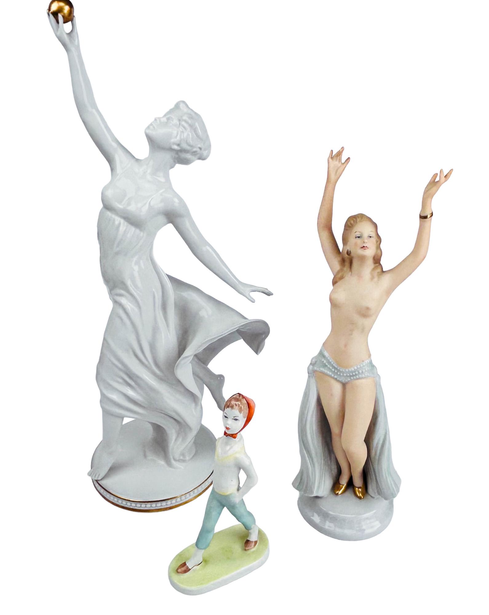 Aquincum Wallendorf Goebel Porcelain Figurine LOT: Estate collection lot of a total of 3 European porcelain figurines. Includes ~ 1 x Aquincum of a young girl with orange head scarf and parasol. 1 x Wallendorf nude exotic cabaret dancer. 1 x Goebel ma
