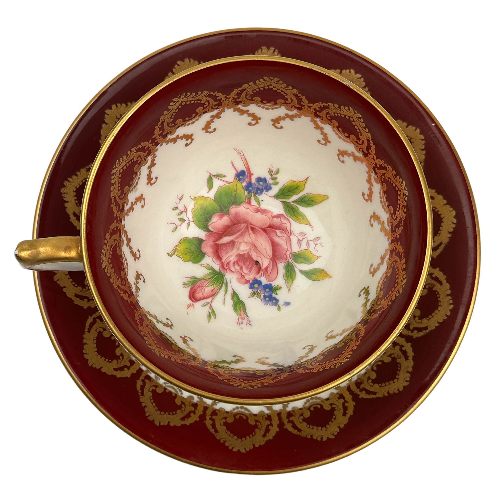 Aynsley Pink Rose Burgundy Gold Trim Cup & Saucer: 20th century England Fine English Bone China tea cup and saucer curio cabinet display. Interior of the cup and the center of the saucer with a pink floral design with blue berries. Burgundy band aroun