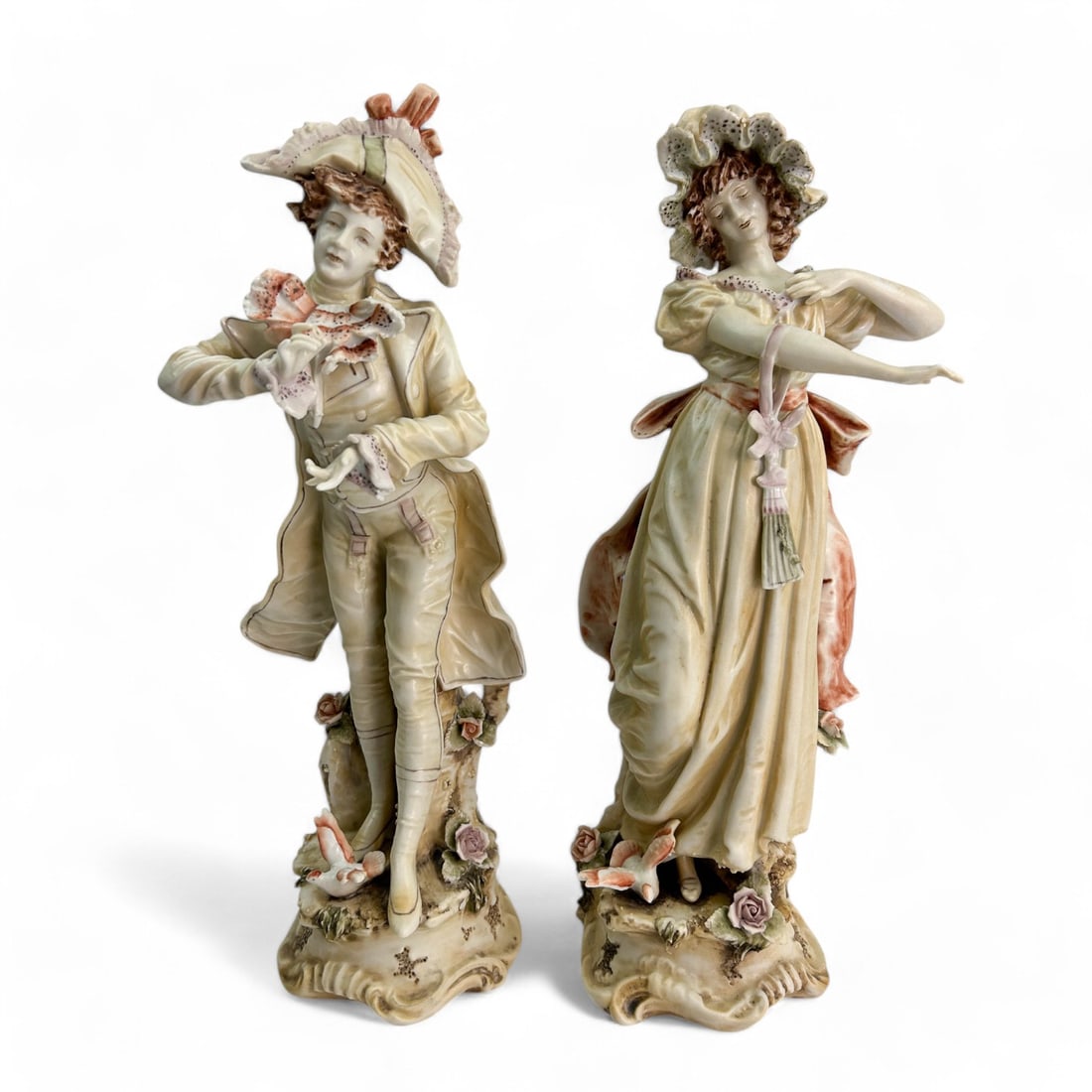 Pair Porcelain Romantic Courting Couple Figurines: Pair of handcrafted and painted porcelain figurines. Features a romantic courting couple, the man dressed in 18th century attire, complete with a detailed jacket and hat adorned with floral accents, t