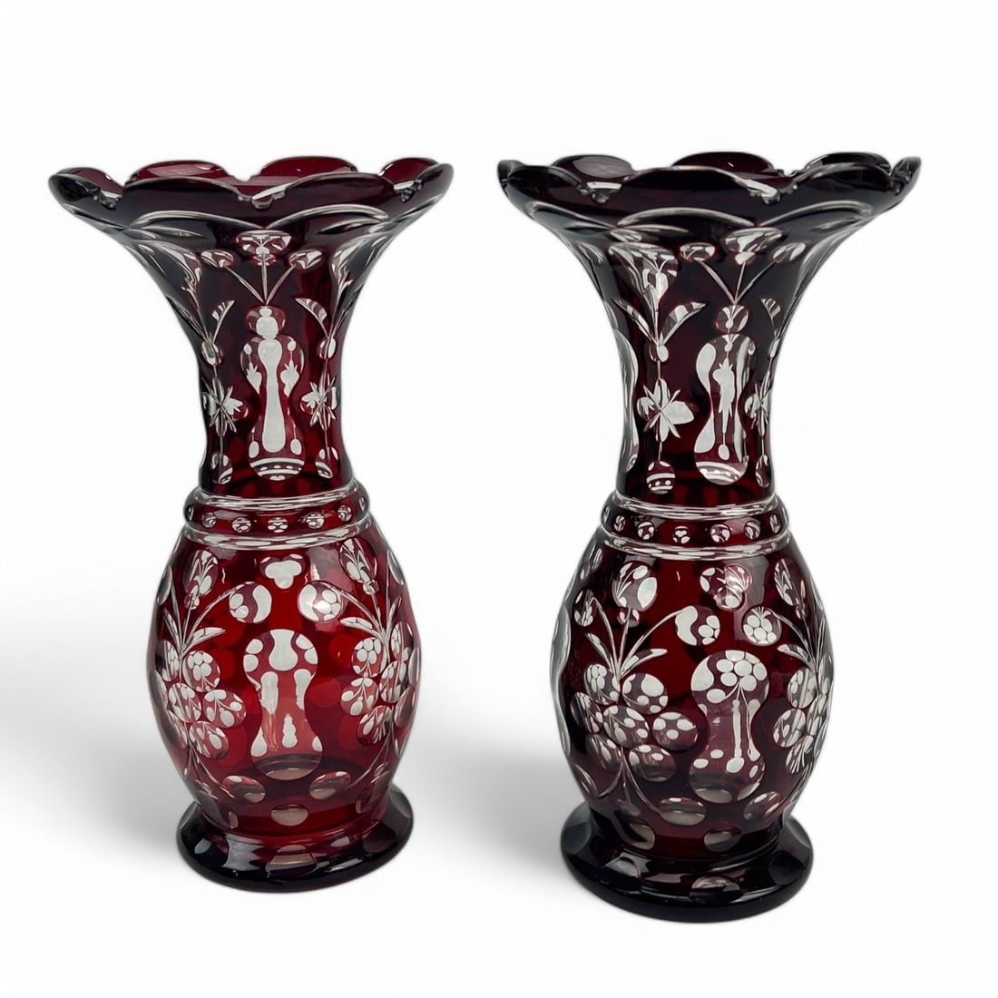 Bohemian Crystal Cranberry Cut Clear Floral Vases: 20th century pair of Bohemian Czech cranberry red cut to clear glass vases. Each features a flared rim with scalloped edges, leading to a finely detailed floral and grapevine motif, hand cut to reveal