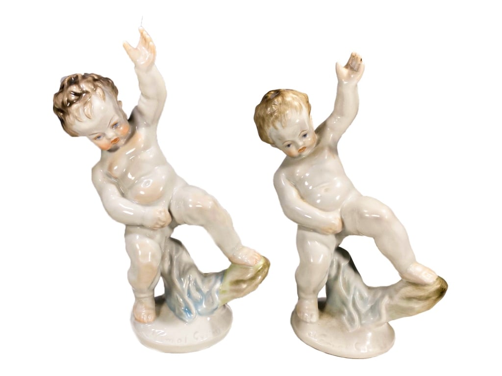 Herend Pair of Hungarian Porcelain Child Figurines: A Herend pair of hand-painted porcelain figures modeled as nude children standing on wave-like bases with their arms raised. Modeled by sculptor Nemes Gyorgy, impressed on its base. Each nears the cla