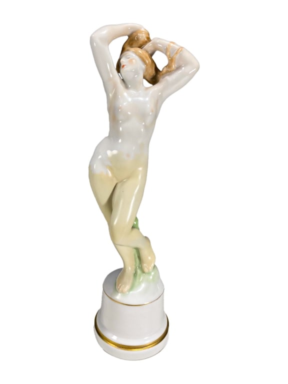 Herend Hand Painted Porcelain Nude Girl Figurine: Herend hand-painted porcelain figurine of a nude female with long flowing hair, posed with both arms raised as she holds her hair. The Hungarian figure stands on a round base accented with a gilt band