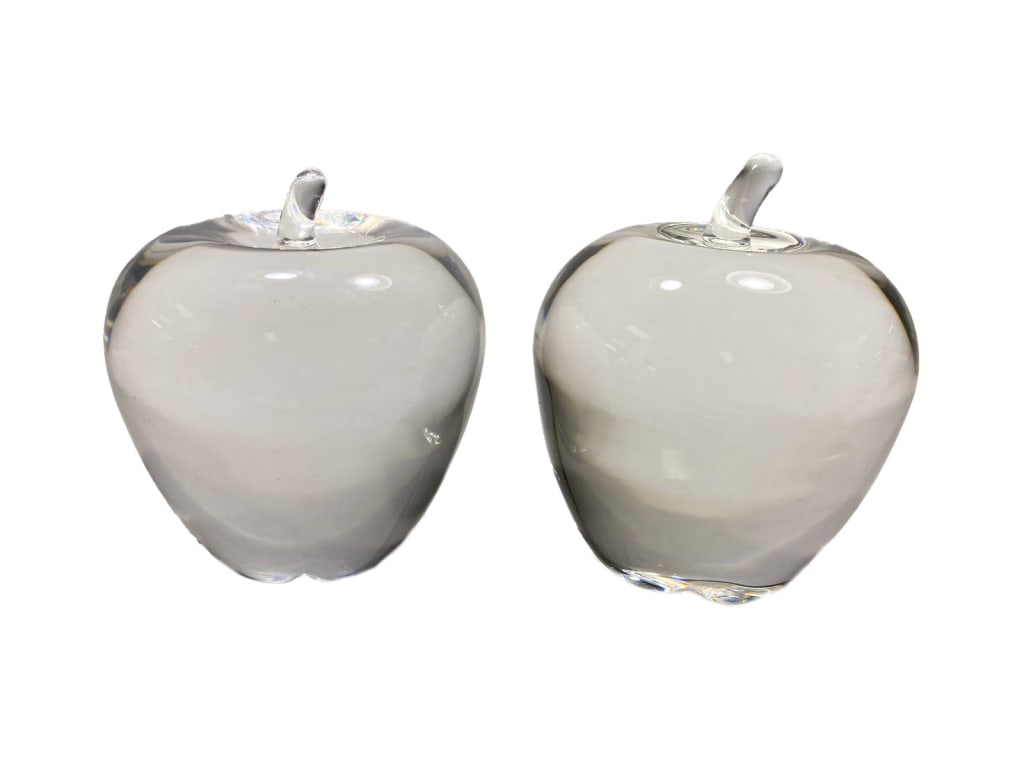 Steuben Crystal Art Glass Apple Paperweights 2pcs: Steuben, pair of clear crystal apple paperweights, each with a pulled-glass stem and star-shaped calyx base. Both are script-signed Steuben. The largest piece measures approximately 4 inches tall by 3