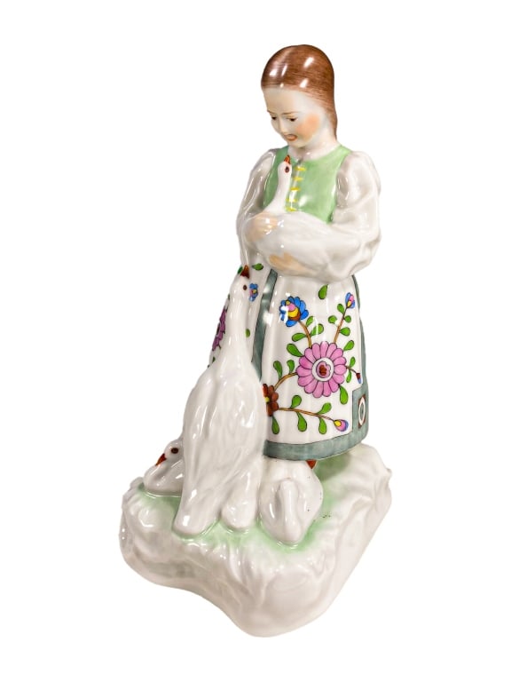 Herend Hungarian Porcelain Girl w/ Geese Figurine: A Herend finely hand-painted porcelain figurine depicting a young girl holding a goose in her arms while two additional geese gather at her feet. The girl wears a traditional Hungarian folk-style cost
