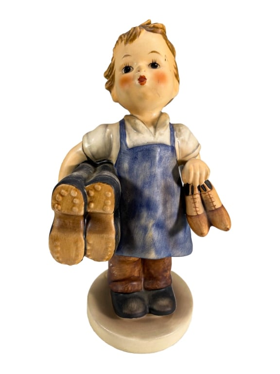Little Shoemaker Porcelain Figurine by M.I. Hummel: M.I. Hummel figurine titled Little Shoemaker, depicting a boy proudly holding menâ€™s and womenâ€™s shoes. Dressed in blue apron and brown trousers. Impressed M.I. Hummel on base, with Goebe