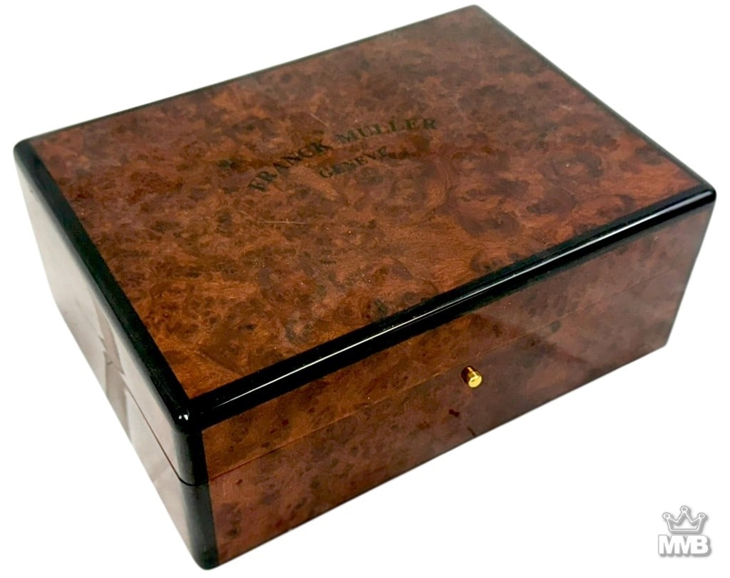 Franck Muller Geneve Luxury Watch Presentation Box: Vintage Franck Muller Geneve wooden watch presentation box, veneered in burlwood with black edge detailing and gilt hardware. The hinged lid opens to reveal a lined interior with Franck Muller Geneve