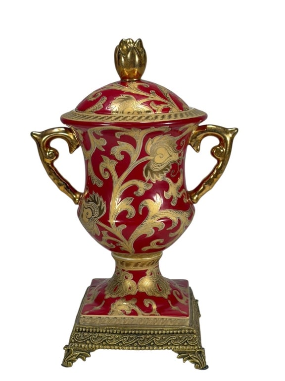 Red & Gilt Lidded Porcelain & Metal Urn: Red and gilt porcelain urn with twin handles, finial lid, and gilt metal base with claw feet. Interior base marked with crowned laurel motif.Dimensions: 11.5 X 7 X 5 in. Condition: Good overall co