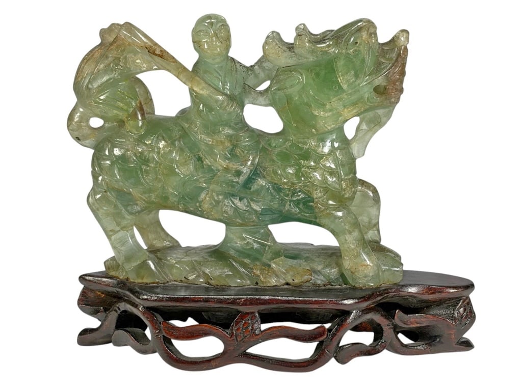 Chinese Carved Fluorite Jade Figurine: Chinese carved fluorite jade figurine of a robed figure riding a qilin, in green tones with natural inclusions. Mounted on pierced wood base. Dimensions: 7.25 X 8.25 X 3 in. Condition: Good overall