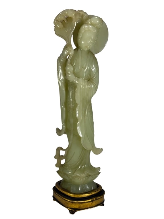 Chinese Carved Jadeite & Wood Figurine: Chinese jadeite figurine of a lady in flowing robes holding a lotus with small animal, mounted on gilt and lacquered wood base.Dimensions: 13 X 3.75 X 2.5 in. Condition: Good overall condition hav
