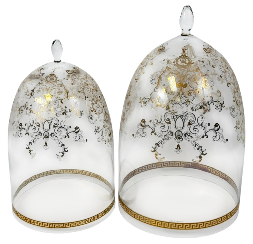 Pair of Versace Rosenthal Gilded Glass Dome Covers: Versace for Rosenthal clear glass dome covers, each piece is beautifully decorated with intricate gold and black baroque scrollwork and a Greek key border along the base. Topped with a clear glass fin