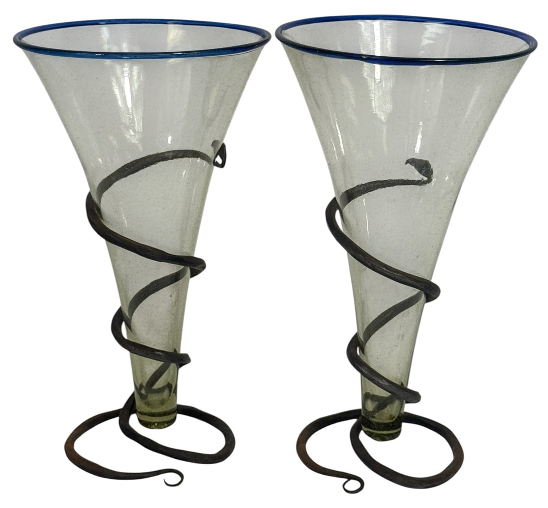 Pair of Blown Glass Vases w/ Wrought Iron Bases: Pair of hand-blown conical glass vases with a faint green tint and applied cobalt blue rims. Each vase is supported by a hand-forged wrought iron spiral base that wraps elegantly around the body and c