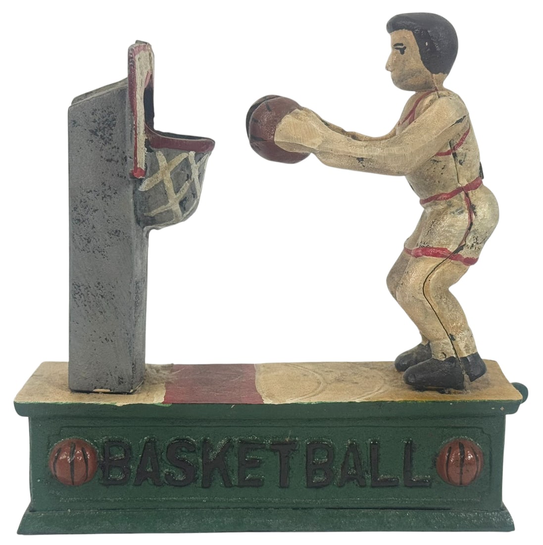 Cast Iron Basketball Player Mechanical Bank: Cast iron, hand-painted mechanical bank depicting a basketball player in mid-shot, poised to dunk the ball into a raised hoop. The green base is labeled 'BASKETBALL' and features molded basketball mot