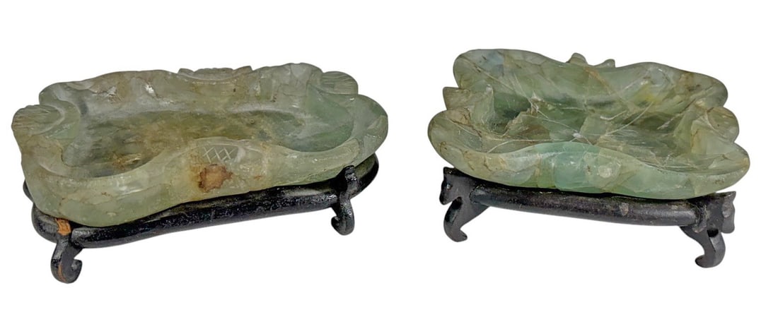 Chinese Carved Fluorite Brush Washers 2pc LOT: Pair of hand-carved fluorite brush washers in mottled pale green with natural inclusions and foliate forms, each mounted on a carved wooden stand. The largest measures approximately 1.5 inches tall by