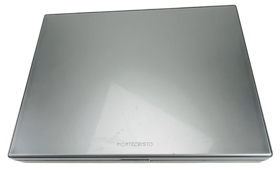 Montecristo Aluminum Cigar Storage Travel Humidor: Rectangular aluminum cigar storage case by Montecristo with hinged lid and front latch. Interior fitted with grooved metal base for cigar placement and black padded panels within the lid. Exterior